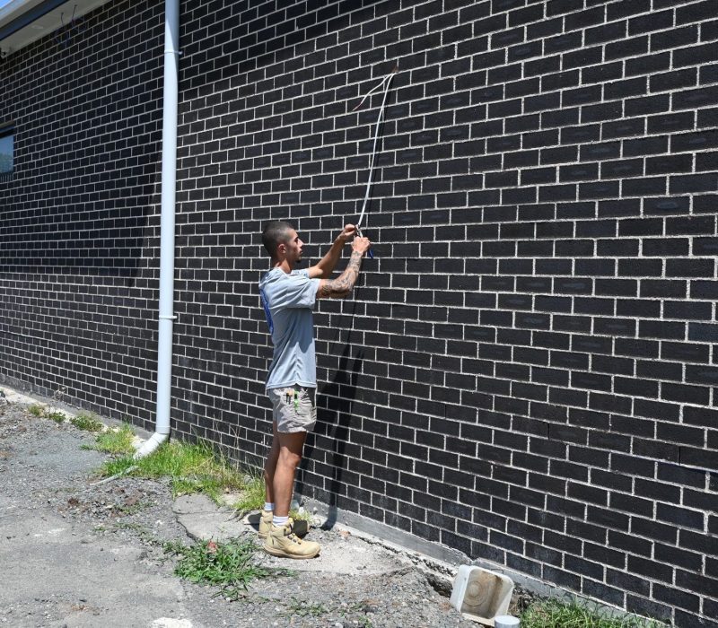 IllaVolt Electrical electrician running electrical cable down an exterior brick wall on a commercial site in the Illawarra