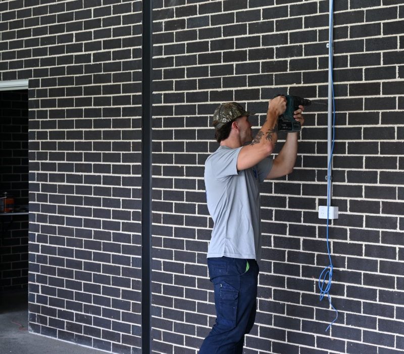 IllaVolt Electrical electrician drilling through brick to run new electrical cable on a Shellharbour build
